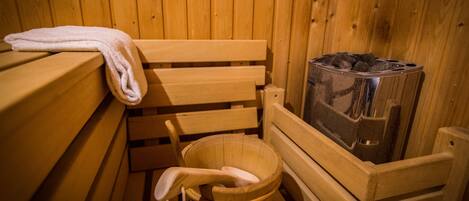 Un banco de sauna de madera con una toalla colgada, un balde de madera y un calentador de sauna.