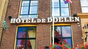 L’extérieur de l’HÔTEL DE DOELEN se caractérise par une façade en briques, de grandes fenêtres et un drapeau.
