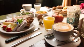Un desayuno con distintos alimentos, una taza de café y un vaso de zumo de naranja sobre una mesa.