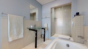 A modern bathroom with a glass sink, a bathtub, and a walk-in shower.