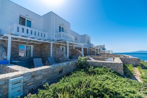 A seaside hotel with white architecture, stone walls, and outdoor seating areas overlooking the ocean. - Cape Mykonos (Mykonos)