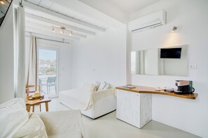 A hotel room with a bed, a desk with a coffee machine, a chair, and a large window. - Cape Mykonos (Mykonos)