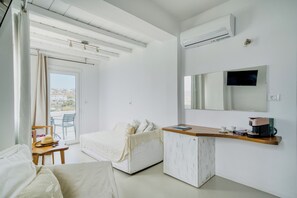 A modern hotel room with a bed, a desk with a coffee maker, a television, and a view of the outdoors. - Cape Mykonos (Mykonos)