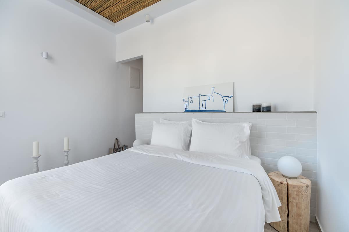 A modern bedroom with a large bed, white bedding, a wooden headboard, and a minimalist wall art piece.