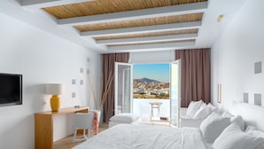 Habitación de hotel moderna con una cama grande, un escritorio y vistas a un paisaje urbano desde un balcón.