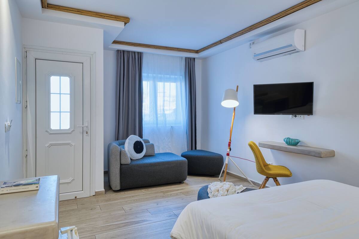 A modern hotel room with a bed, a desk, a TV, a chair, and a sofa.
