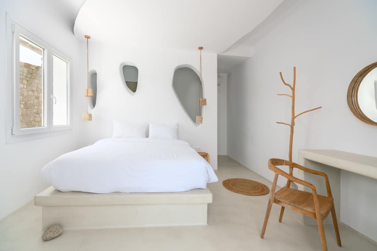 A minimalist bedroom with a large bed, a wooden chair, and a mirror on the wall.