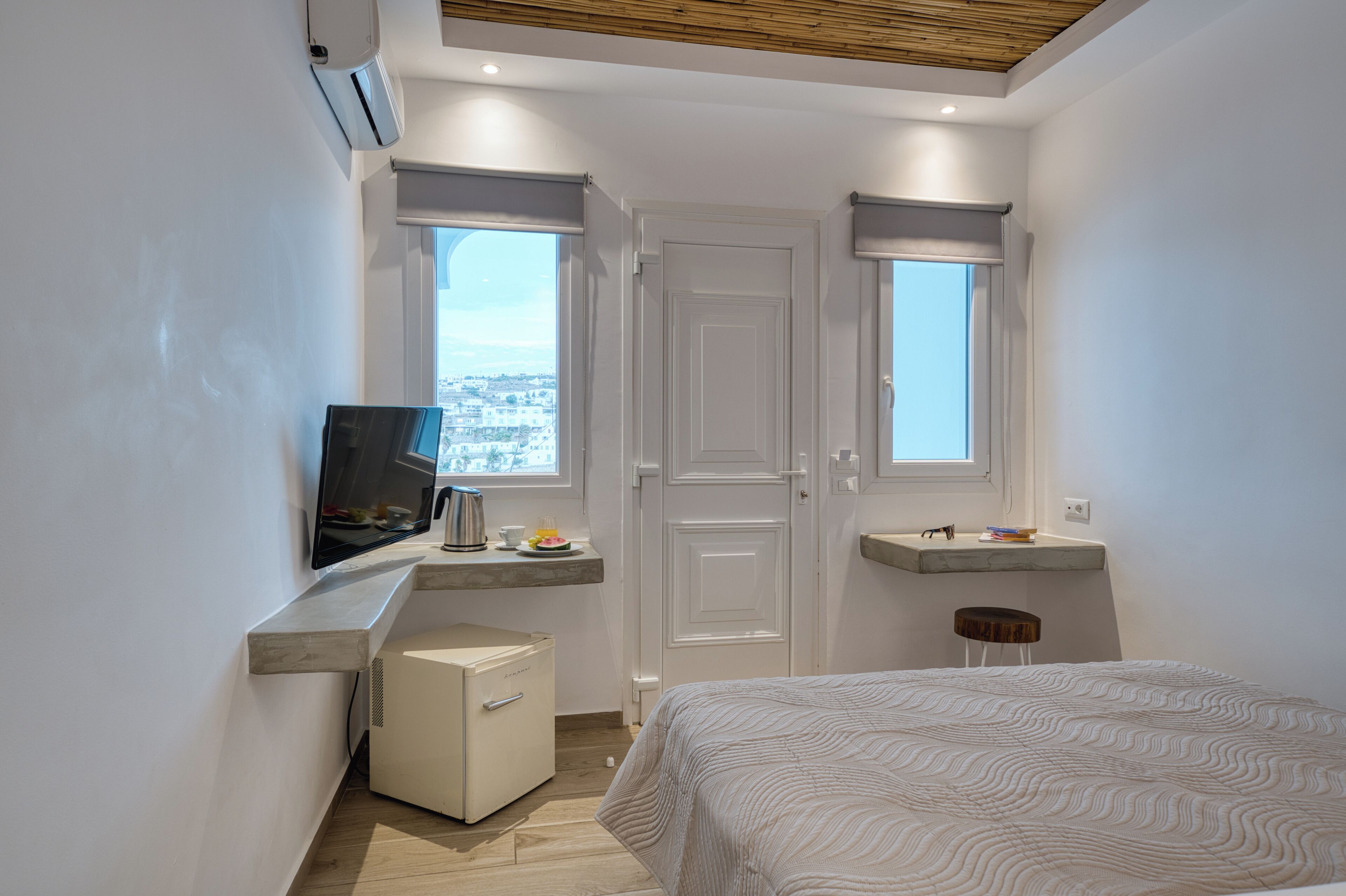 Une chambre moderne avec un lit, une télévision, un petit bureau et une fenêtre donnant sur la ville.