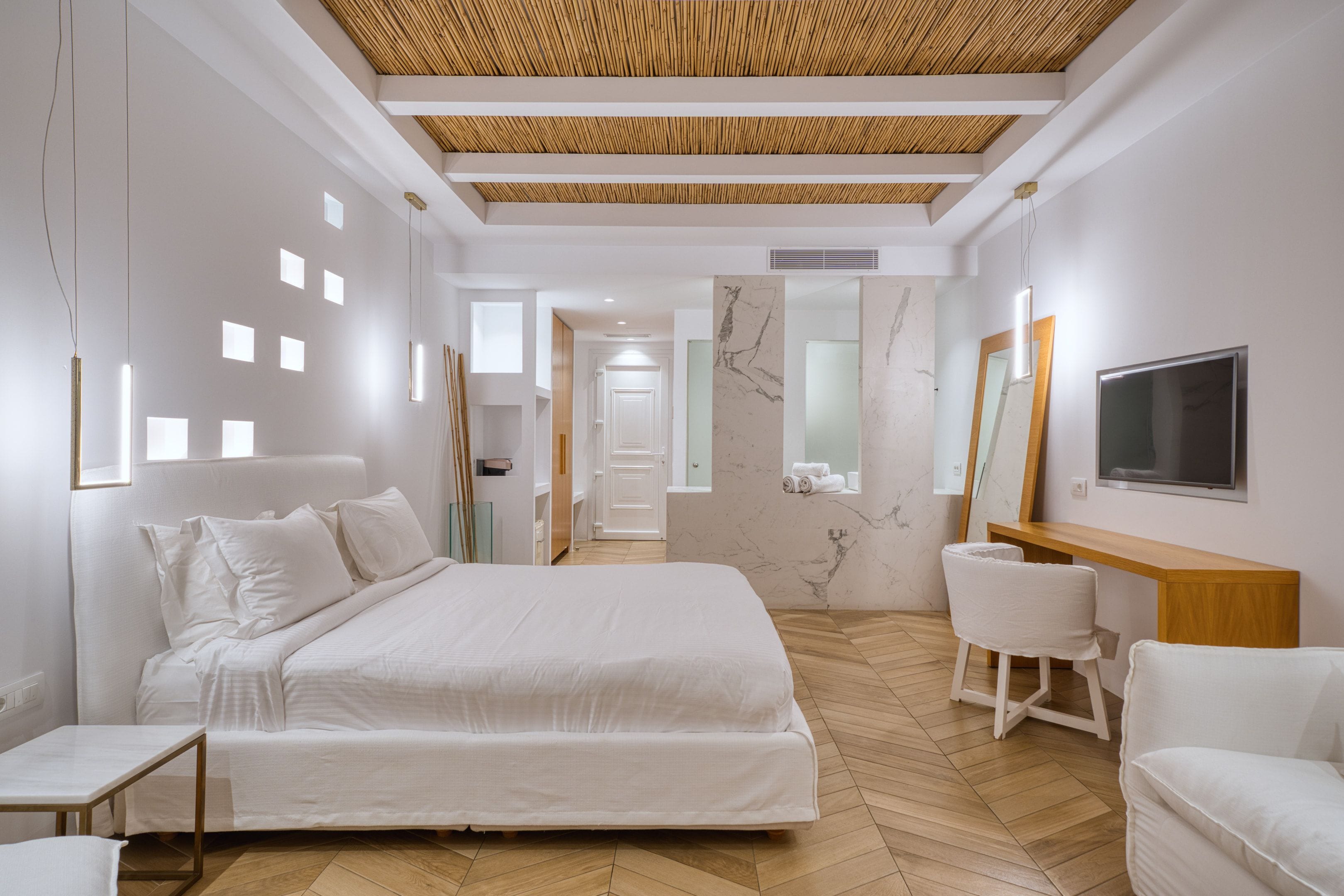 A modern hotel room with a large bed, a desk, a chair, and a TV.
