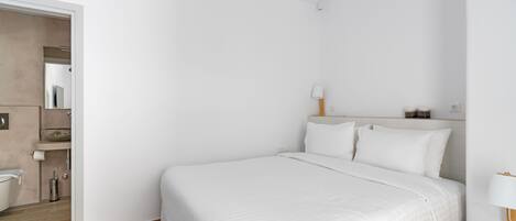 A modern hotel room with a large bed, a bedside table with a lamp, and a bathroom visible through an open door.