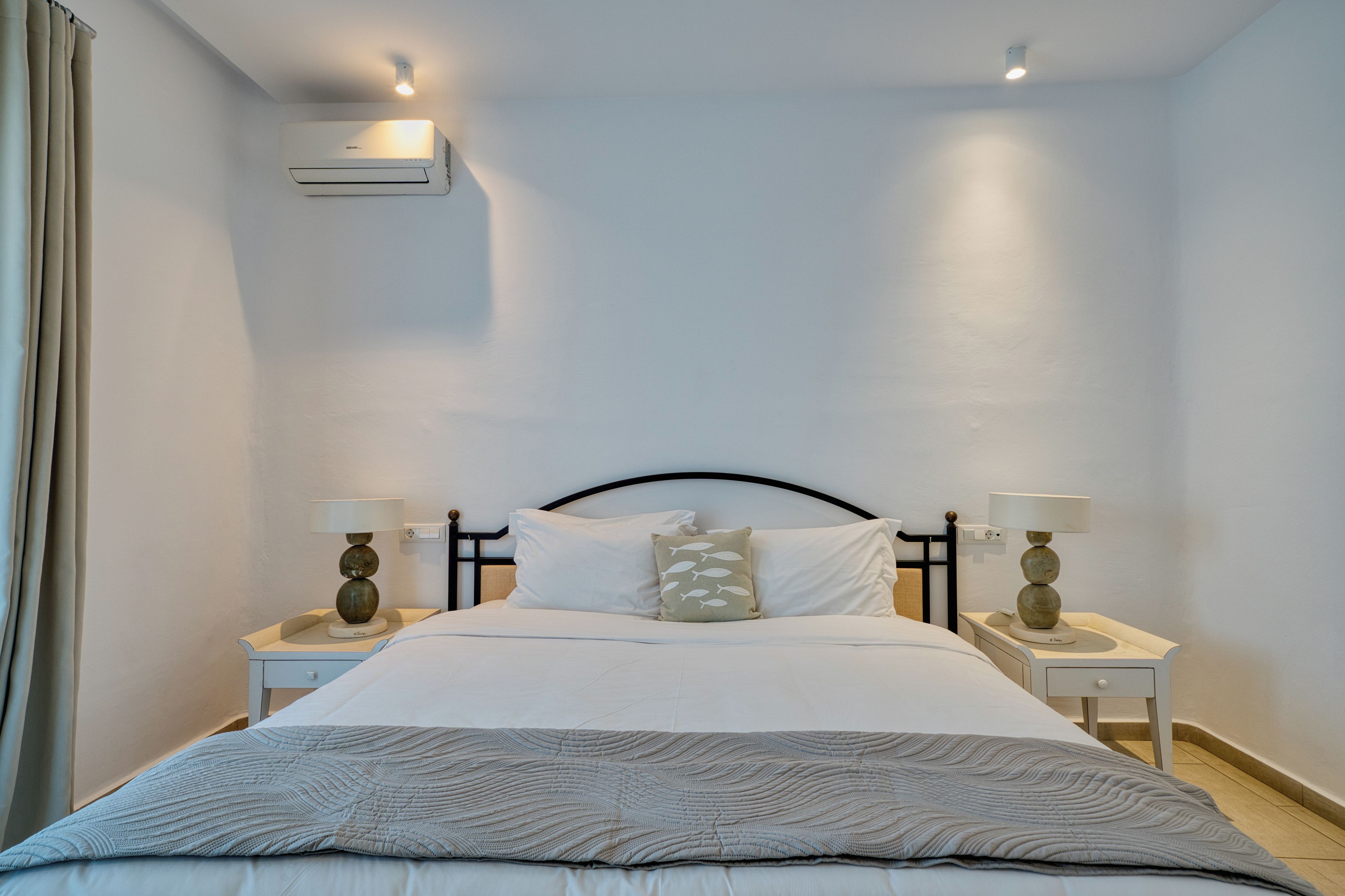 Una habitación de hotel con una cama, dos mesitas de noche, aire acondicionado de pared y una ventana con cortinas.