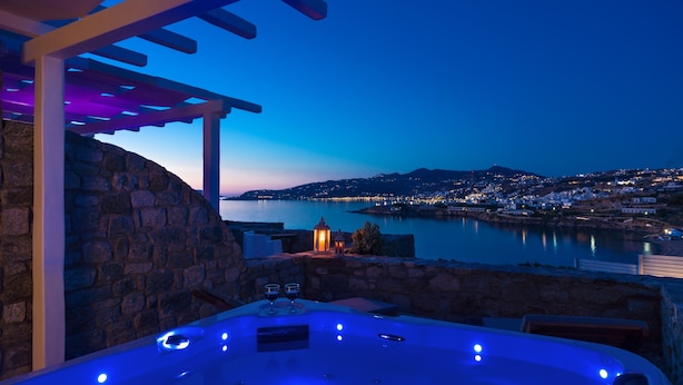 Un jacuzzi con pared de piedra y vista a un cuerpo de agua al atardecer.