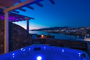 A hot tub with a stone wall and a view of a body of water at dusk. - Cape Mykonos (Mykonos)