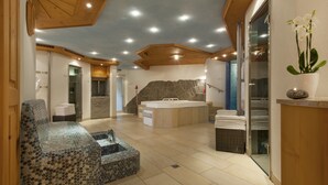 A spacious spa area with a large bathtub, a seating area with a mosaic design, and a wooden ceiling.