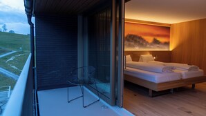 A modern bedroom with a large bed, a chair, and a view of a sunset through a glass door.