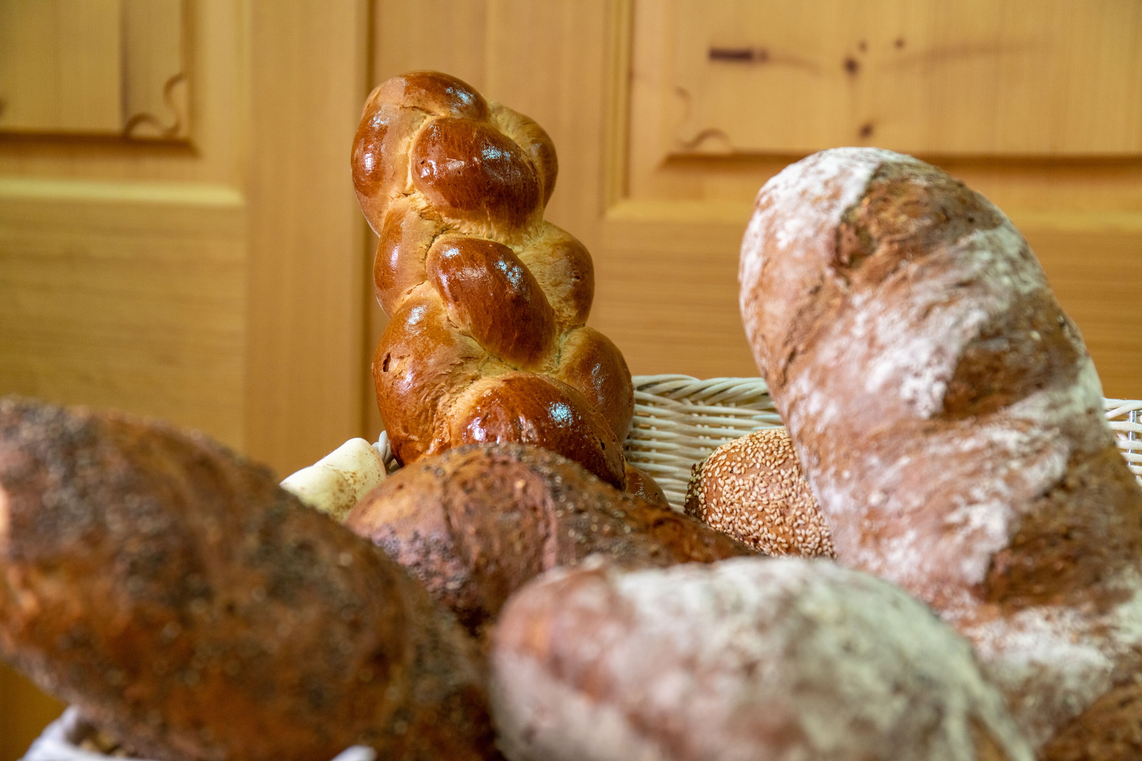 A variety of breads, including a braided loaf and a round loaf with sesame seeds, displayed on a table.