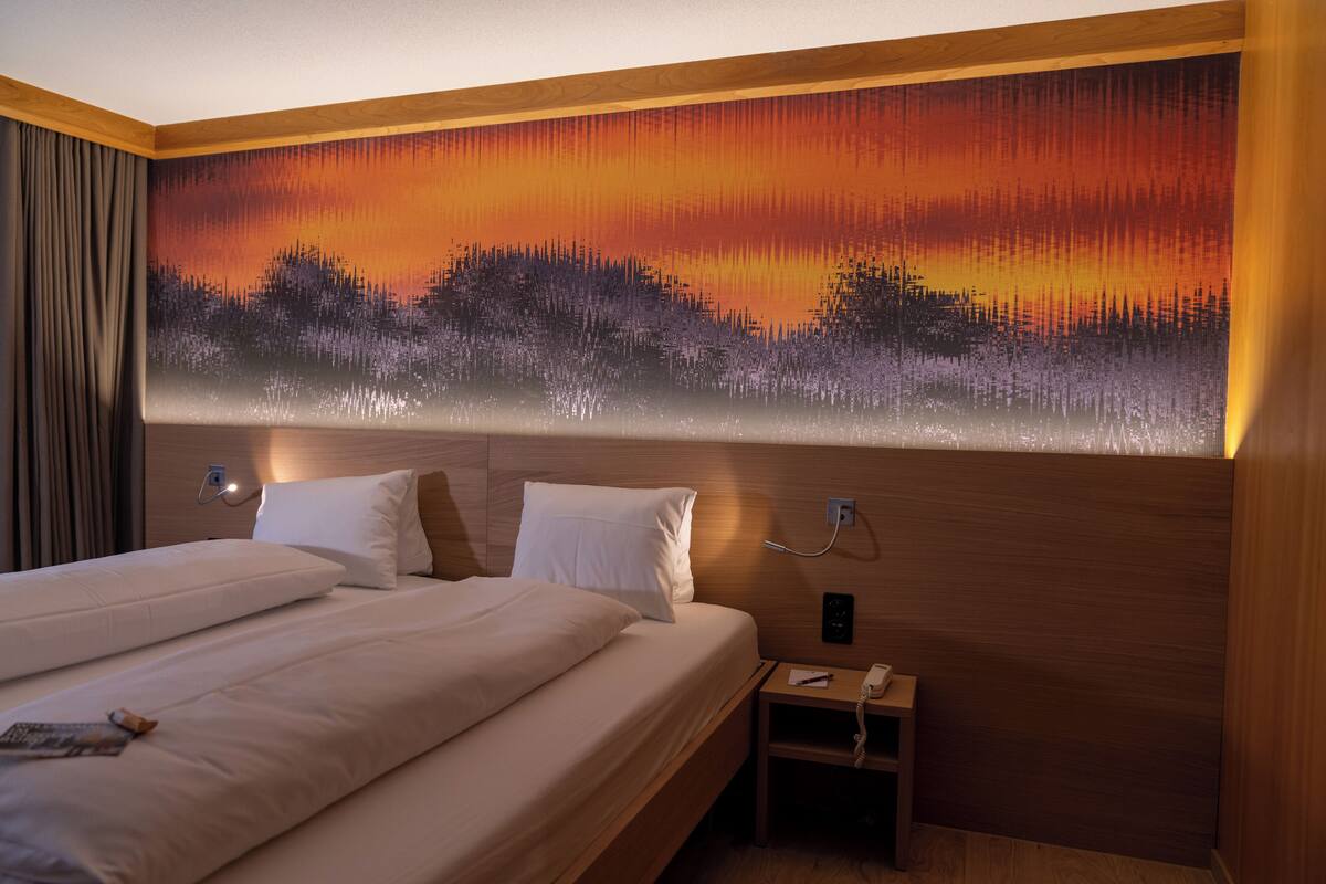Een hotelkamer met een groot bed, een nachtkastje en een wanddecoratie van een zonsondergang.