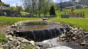 A small waterfall in a grassy area with rocks and a few chairs.