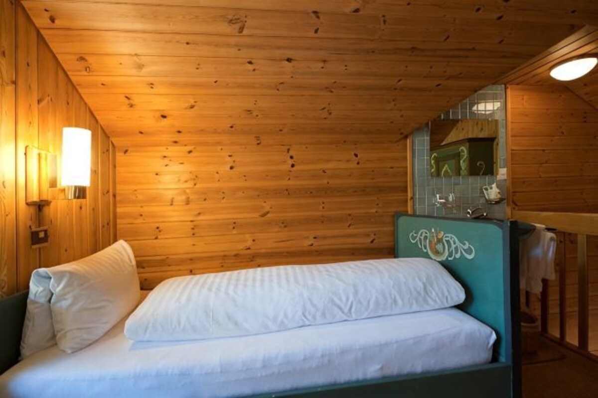 A wooden-paneled room with a bed, a wall-mounted light, and a mirror.