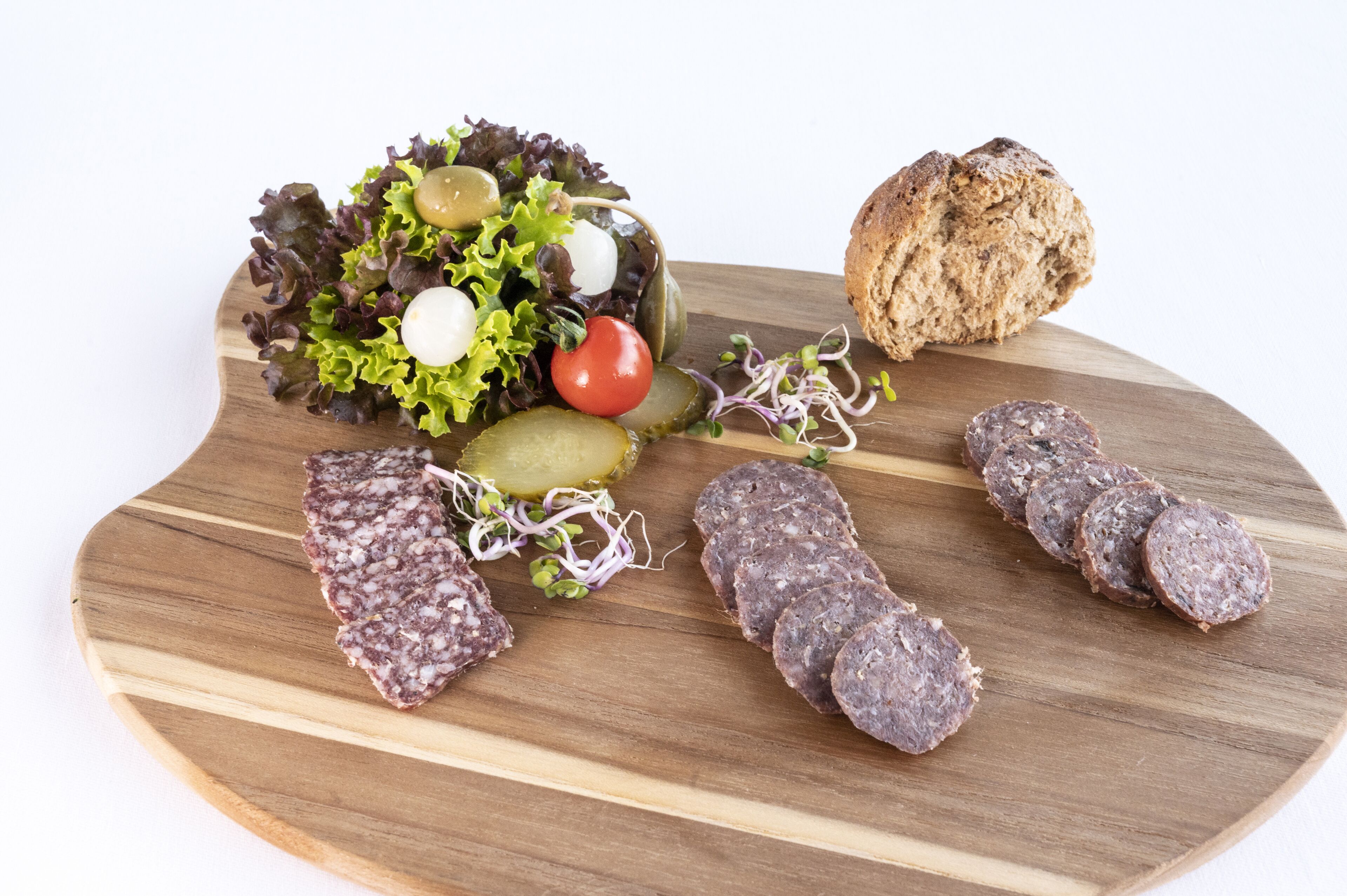 Ein Holzbrett mit verschiedenen Lebensmitteln, darunter geschnittene Salami, Gurken, ein Brotlaib, ein Salat mit Salat, Tomaten und Oliven.