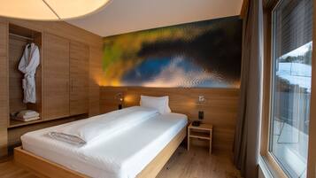 Une chambre d’hôtel moderne avec un lit en bois, un grand tableau abstrait accroché au mur et une vue sur un paysage enneigé par la fenêtre.