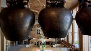 A restaurant with large hanging pots, wooden tables, and chairs.