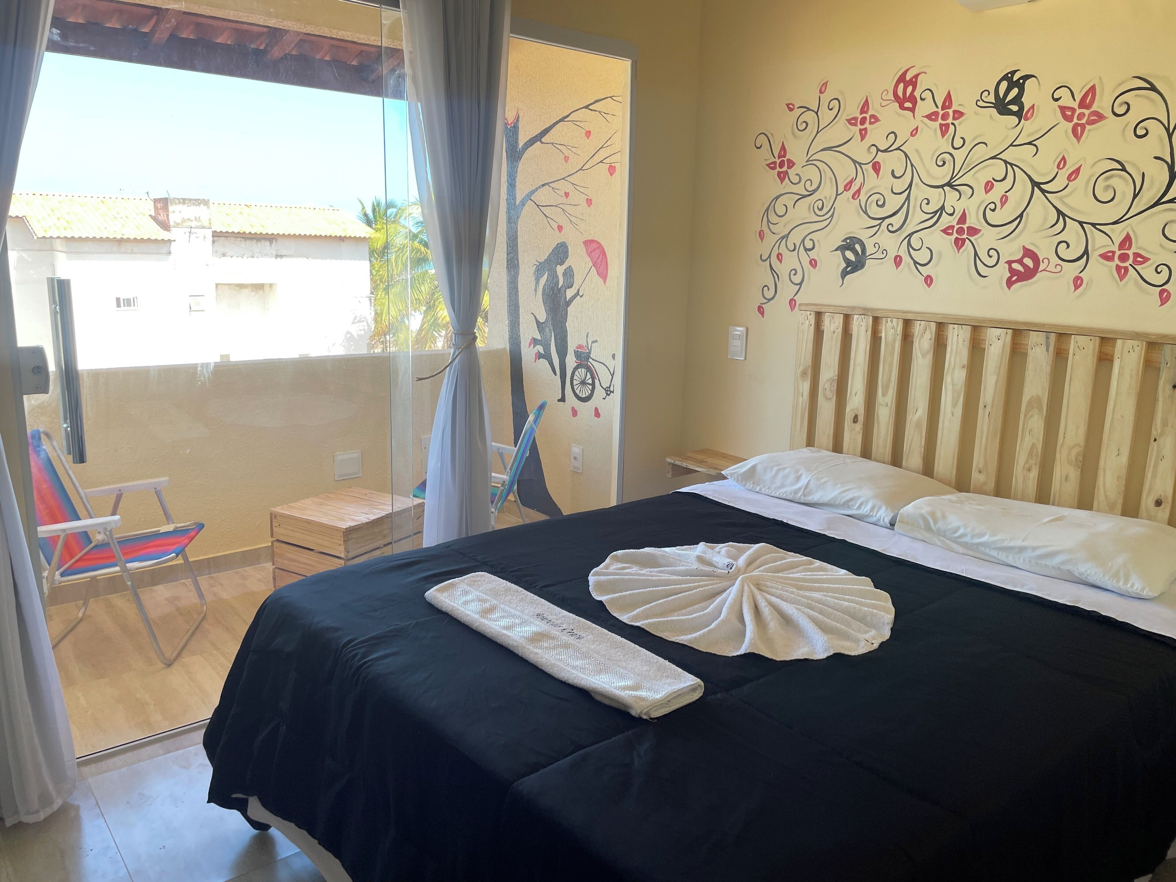 A bedroom with a black bedspread, white pillows, and a decorative wall mural.