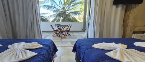 Habitación de hotel con dos camas, un balcón con mesa y sillas, y vista a palmeras.