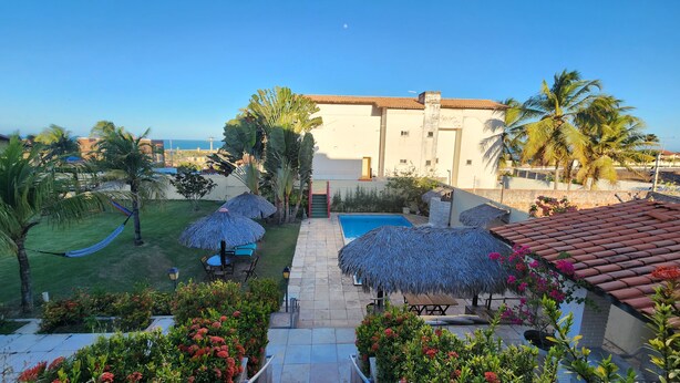 A pool area with a thatched umbrella, a hammock, and a view of the sea. - Pousada Ceará Porto das Dunas (Aquiraz)