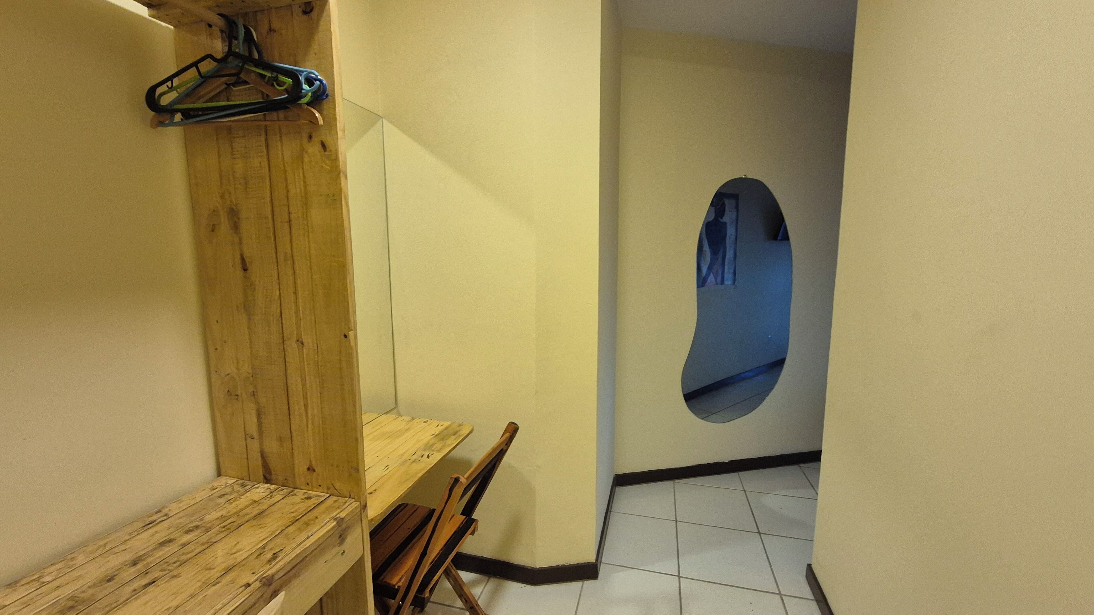 A narrow hallway with a wooden bench, a coat rack, and a wall-mounted mirror.