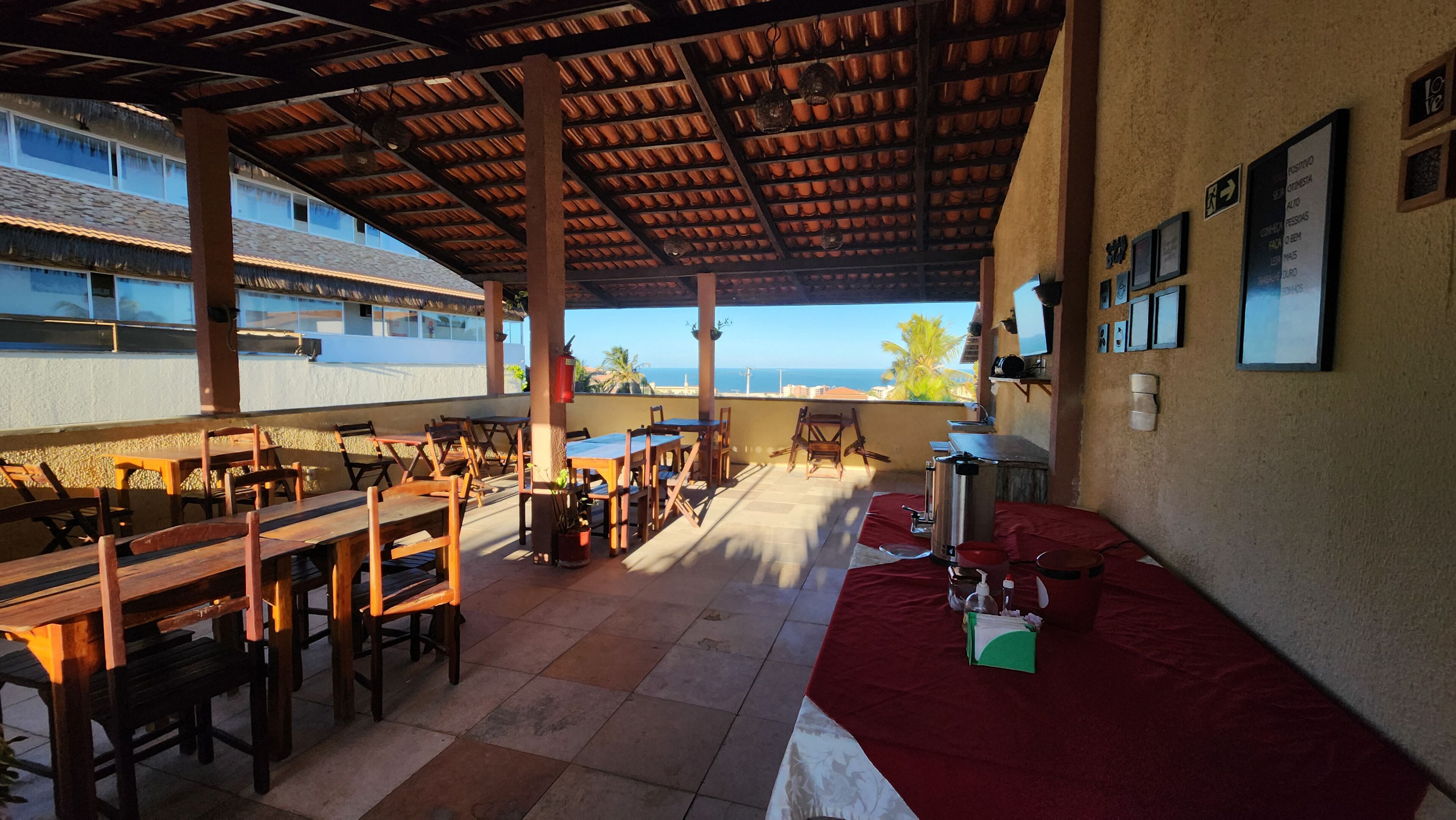 Un espace de restauration en plein air avec des tables et des chaises en bois, un canapé recouvert d’un tissu rouge et une vue sur l’océan.