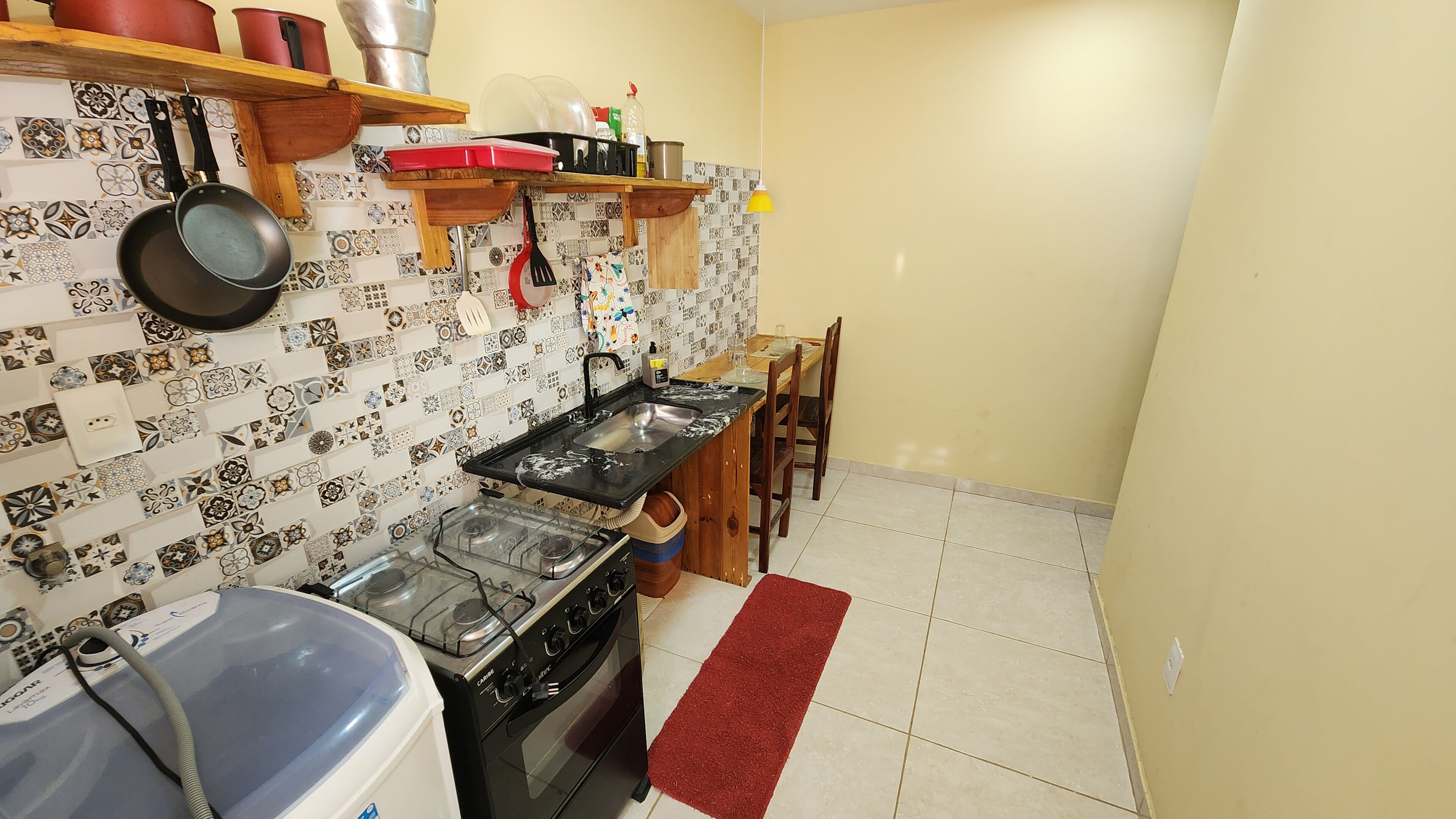 Cocina compacta con estufa a gas, un lavamanos y diverso menaje y utensilios de cocina en la pared.