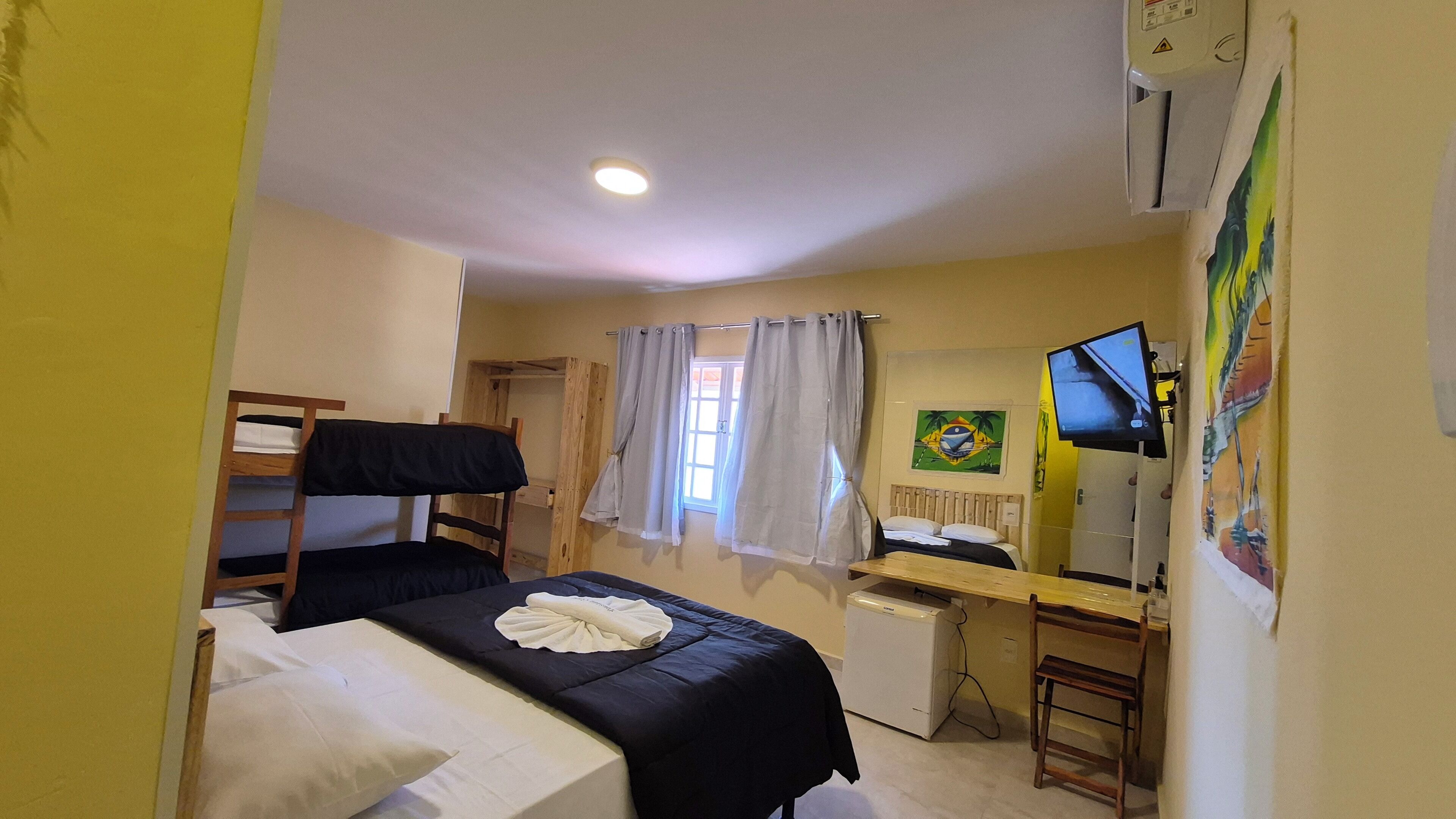 A room with bunk beds, a desk, a chair, a television, and a window with curtains.