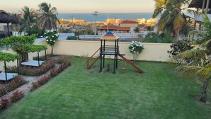 A rooftop garden with a play structure, a small seating area, and a view of the cityscape and ocean. - Pousada Ceará Porto das Dunas (Aquiraz)