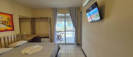 Habitación de hotel con una cama, televisión montada en la pared, un cuadro y vistas al exterior a través de la ventana.
