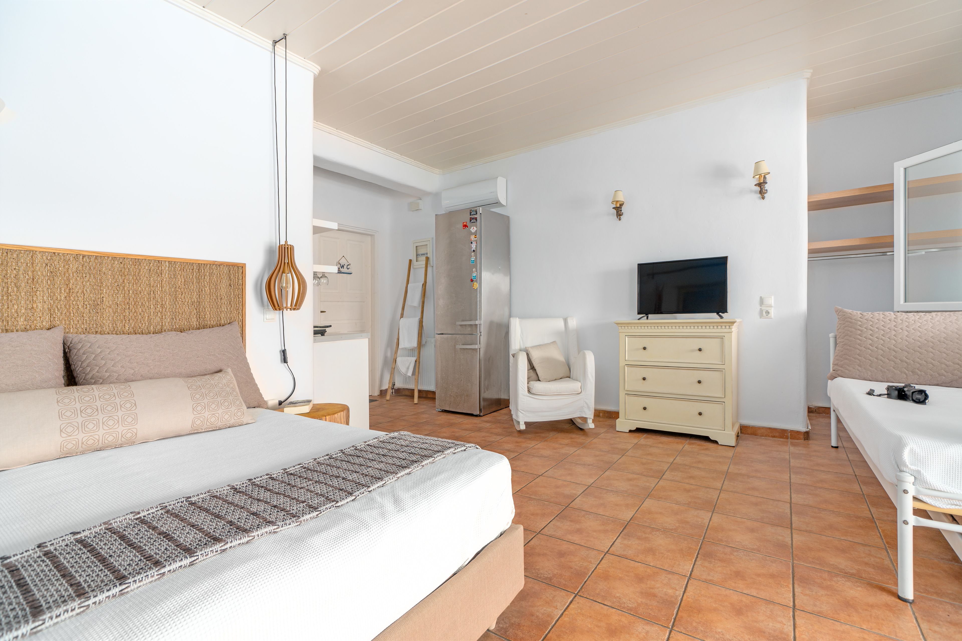 Una camera da letto con un letto, una cassettiera, una sedia, un televisore e un frigorifero.