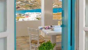 A balcony with a table and chairs, a view of the sea and a hilly landscape, and a blue door frame. - Ornos Blue (Mykonos)