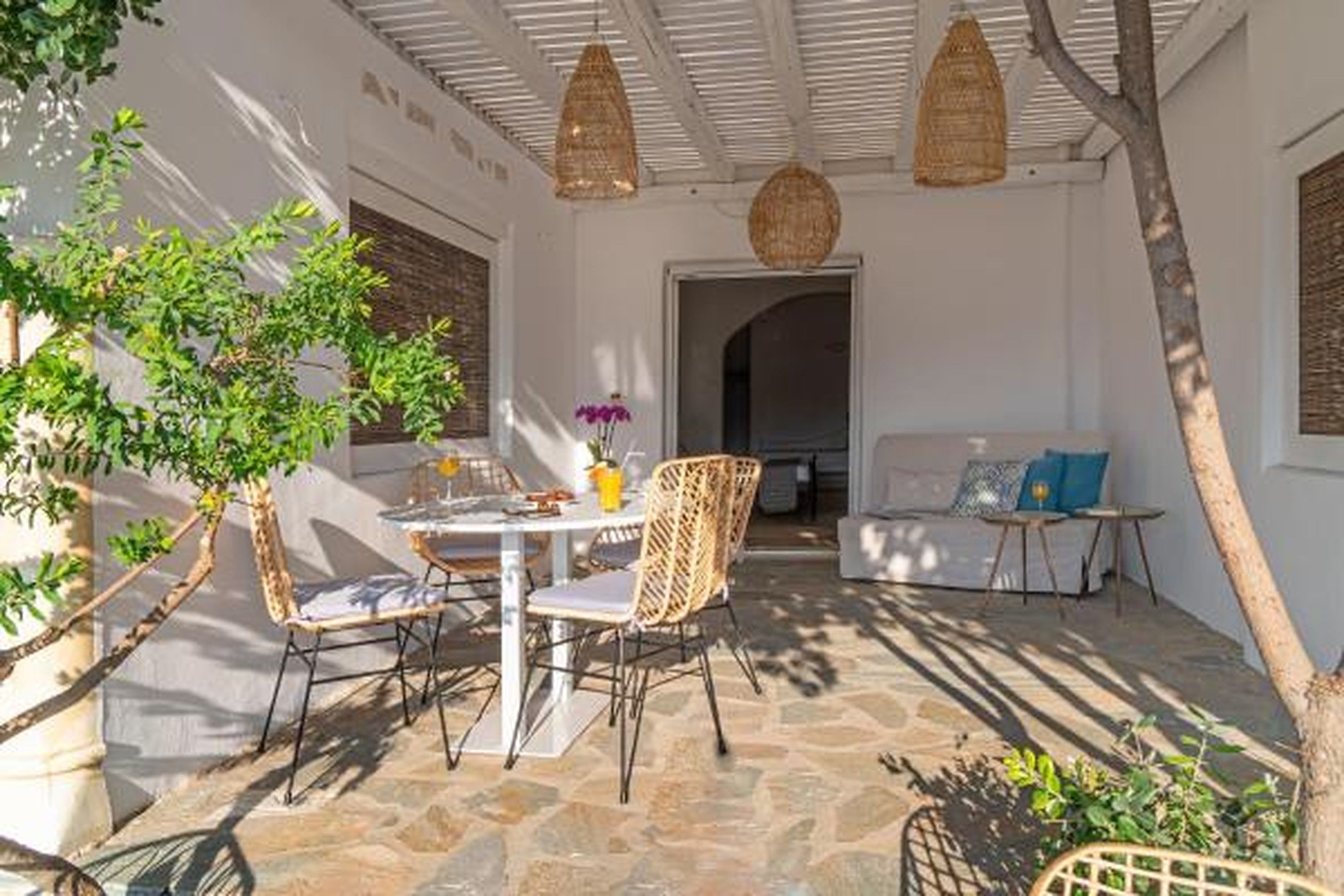 Un patio exterior con suelo de piedra, mobiliario de mimbre y un sofá blanco.