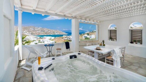 A rooftop terrace with a hot tub, outdoor seating, and a view of the sea and buildings. - Ornos Blue (Mykonos)