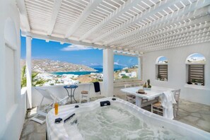 A rooftop terrace with a hot tub, outdoor seating, and a view of the sea and buildings. - Ornos Blue (Mykonos)