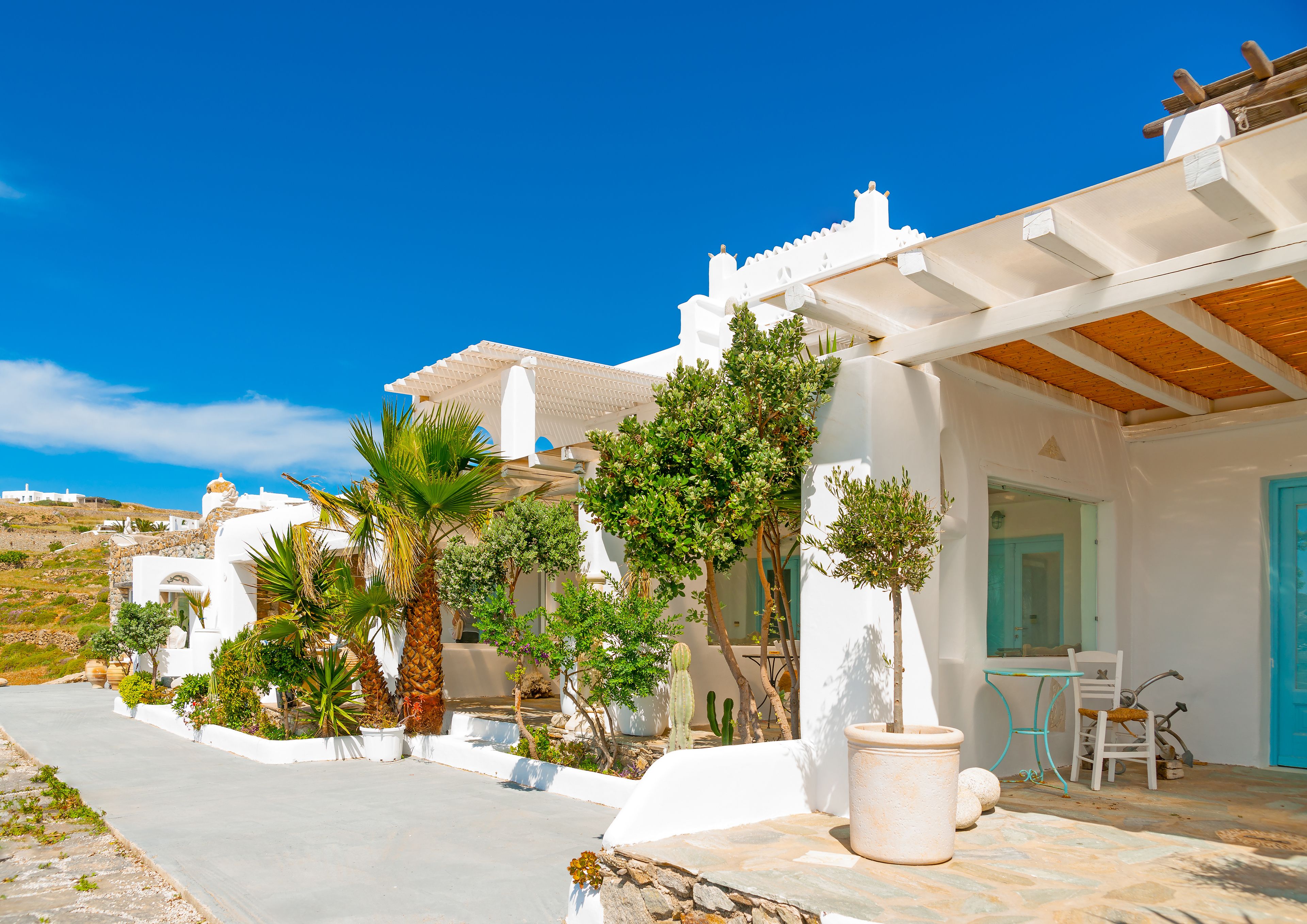 A coastal building with white walls, a wooden pergola, and a stone pathway.