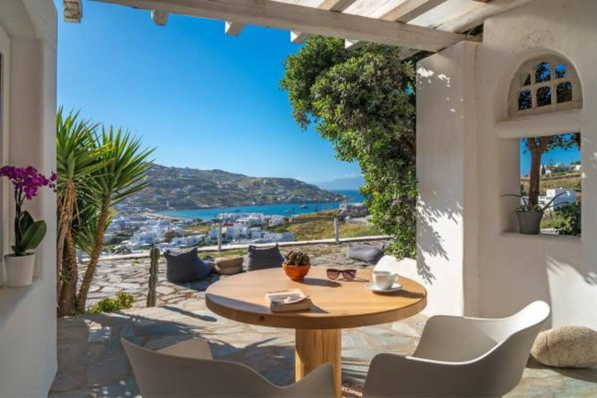 Una mesa redonda con sillas, una planta en maceta y vistas de un paisaje costero con edificios y montañas.