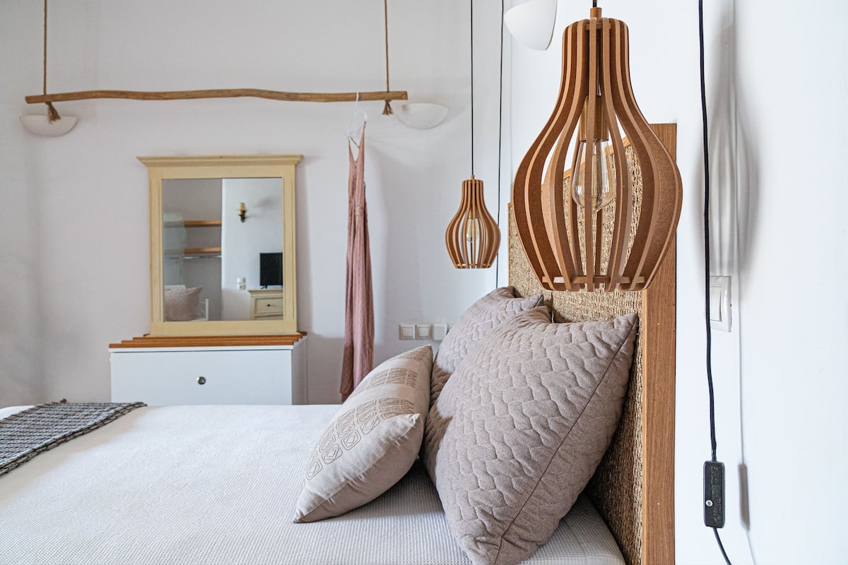 Un dormitorio con cama, cabecero de madera, espejo y dos lámparas colgantes.