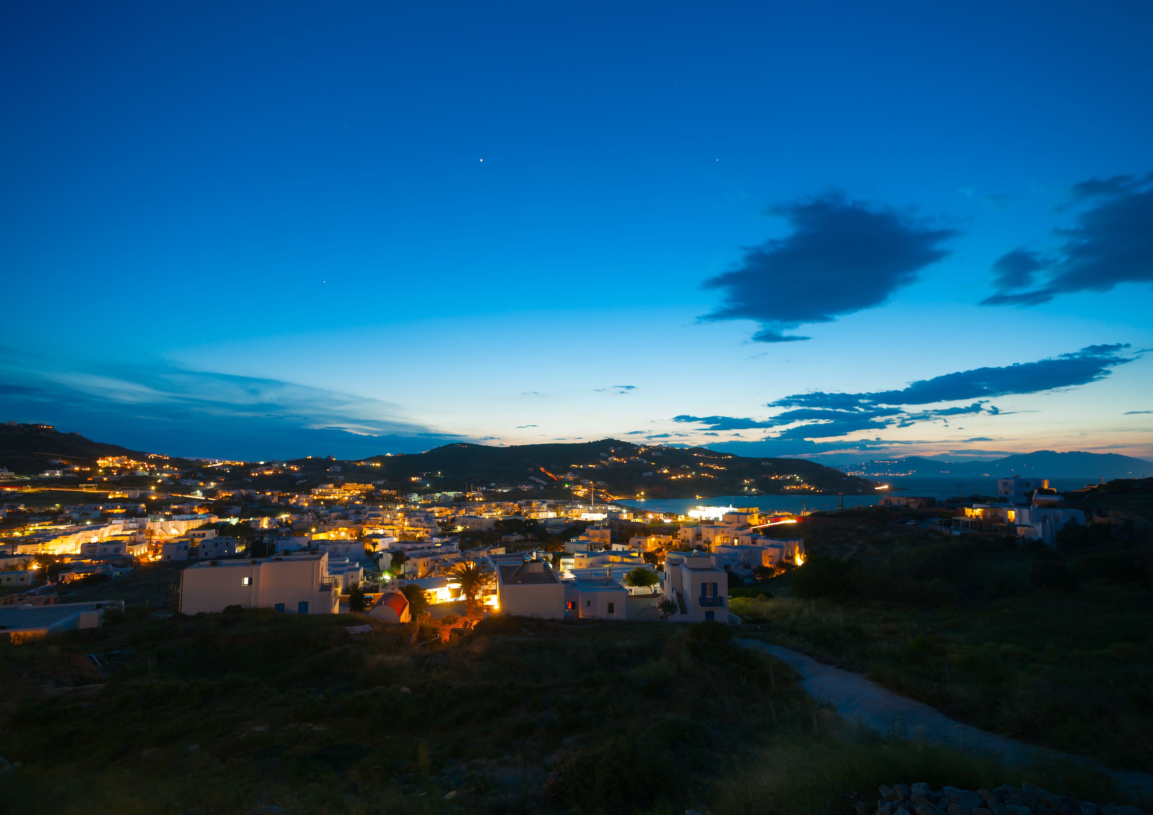 A coastal town at dusk with illuminated buildings and a clear view of the sea.