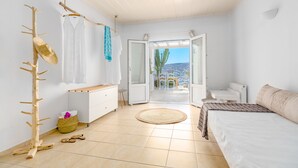 A bedroom with a bed, a wooden drying rack, a white dresser, and a view of a cactus garden through an open door. - Ornos Blue (Mykonos)