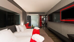 Una habitación de hotel moderna con una cama grande, una pared de acento roja y un televisor de pantalla plana montado en la pared.