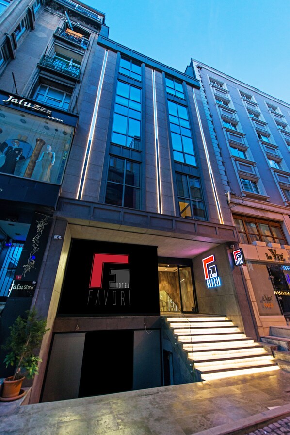 Facciata moderna di un hotel con un evidente cartello 'FAVORI', ampie finestre e una scala che conduce all'ingresso.