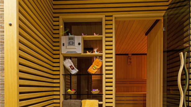 Un sauna con listones de madera, un banco, una toalla y un estante pequeño con objetos.