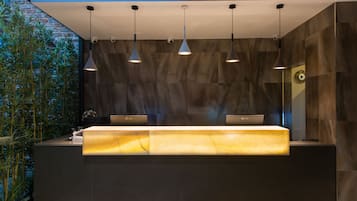 Un comptoir d’accueil au design moderne, doté d’un plan de travail foncé et de trois luminaires suspendus au-dessus.