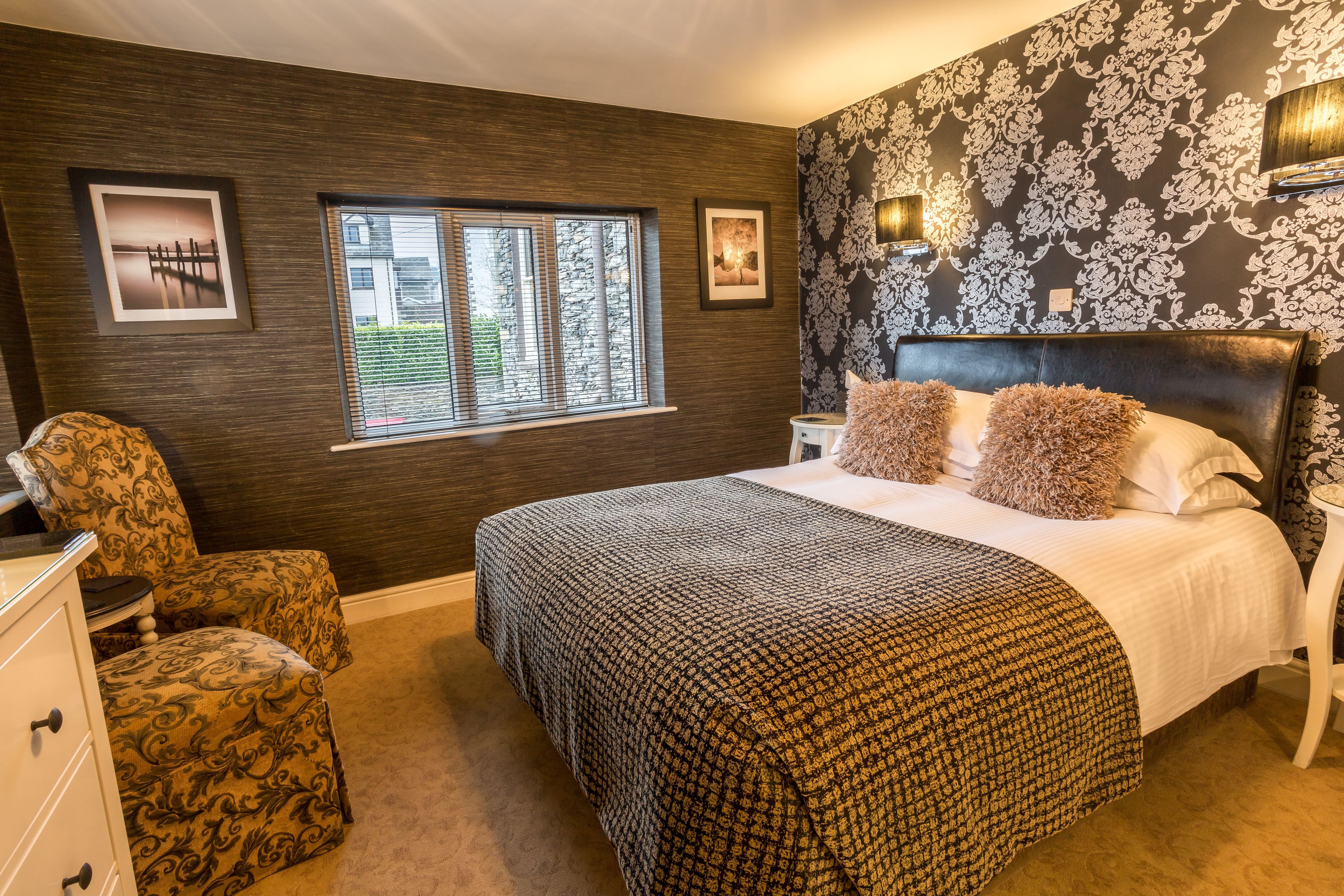 A bedroom with a large bed, a chair, a dresser, a window, and a wall with a floral pattern.